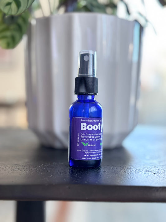 BootyMist toilet paper spray bottle displayed on an outdoor table in front of a modern silver planter — a clean, natural solution for transforming toilet paper into a refreshing, flushable wipe.