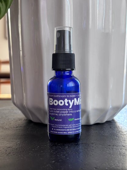BootyMist toilet paper spray bottle displayed on an outdoor table in front of a modern silver planter — a clean, natural solution for transforming toilet paper into a refreshing, flushable wipe.