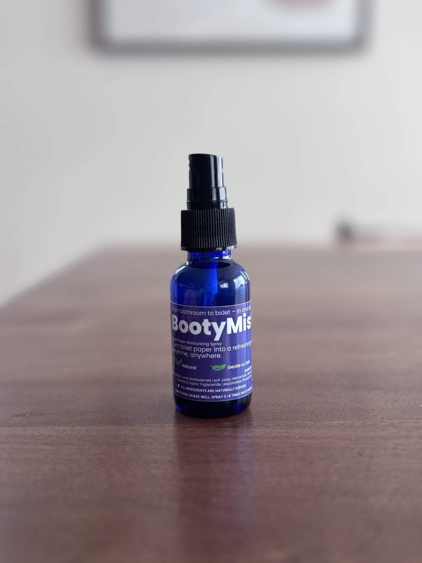 BootyMist toilet paper spray bottle standing on a wooden table with soft background — flushable wipe alternative for gentle, everyday use.
