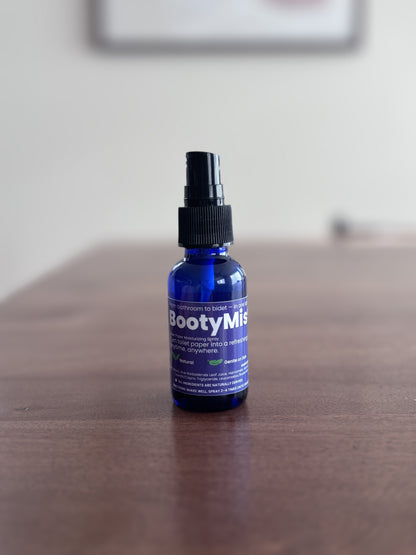 BootyMist toilet paper spray bottle standing on a wooden table with soft background — flushable wipe alternative for gentle, everyday use.